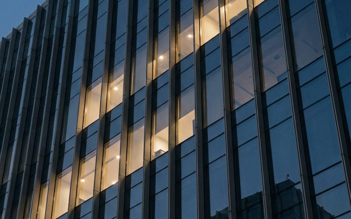 Glass and steel office facade at dusk with lit floors behind the windows