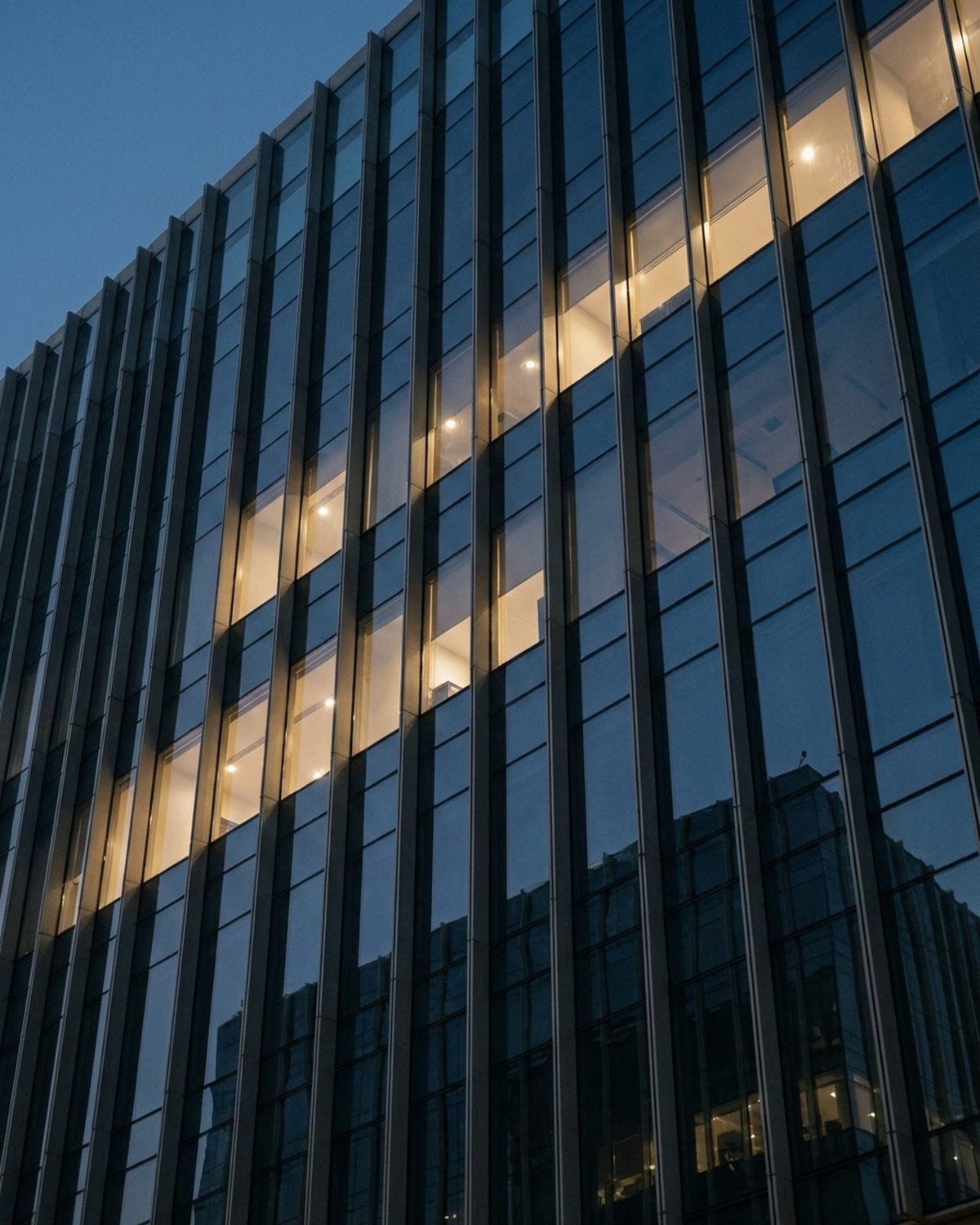 Glass and steel office facade at dusk with lit floors behind the windows