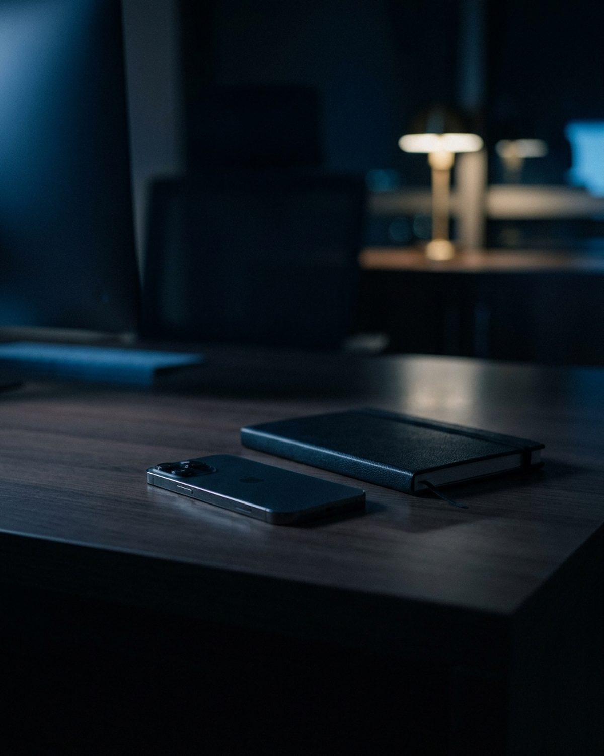 A phone lying face down beside a closed notebook on a desk at night